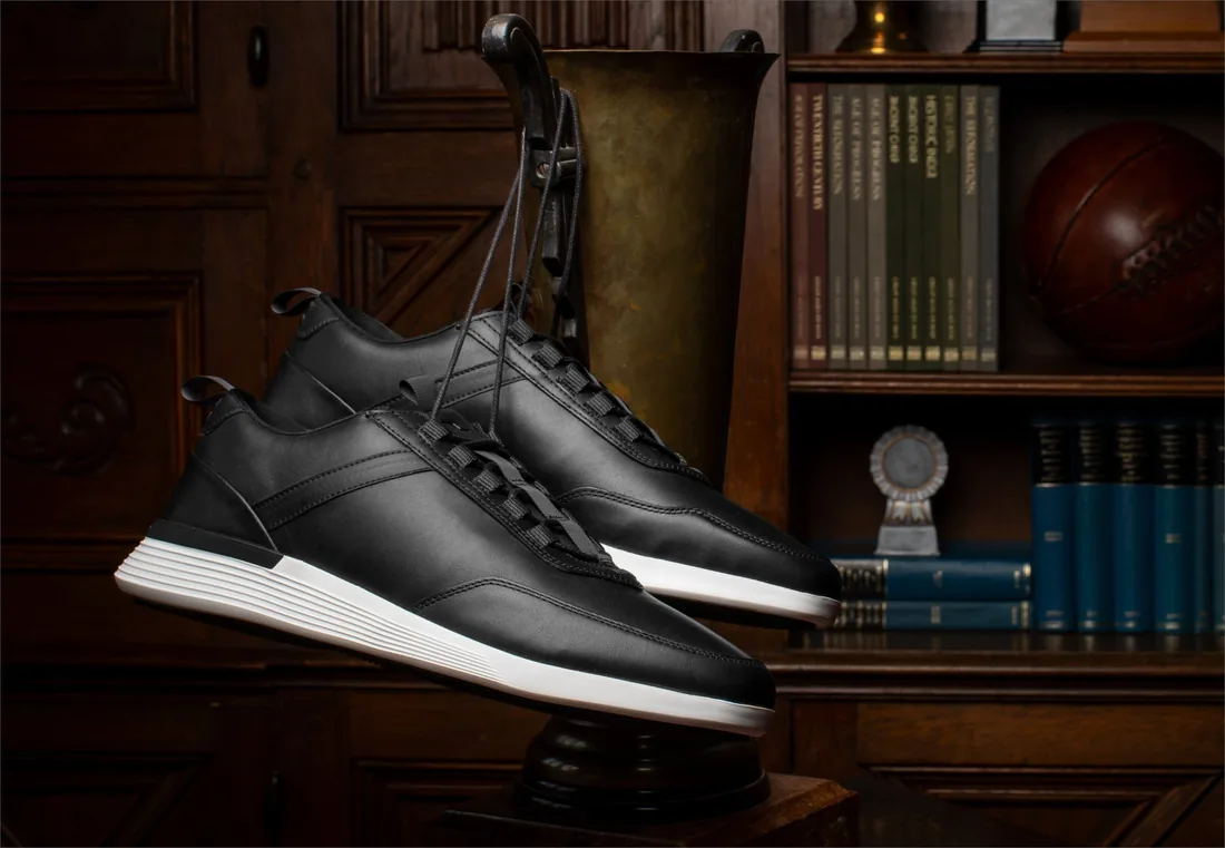A pair of jet black Crossover Victory Trainers displayed on a wooden shelf in a panelled study
