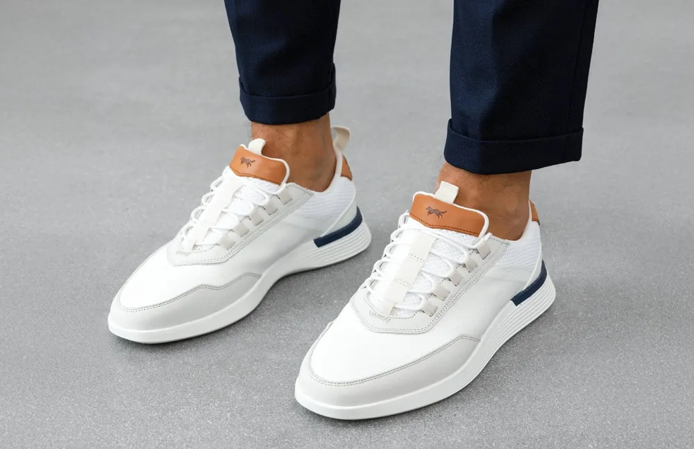 White Crossover Victory Trainers worn with navy trousers, standing on a concrete floor